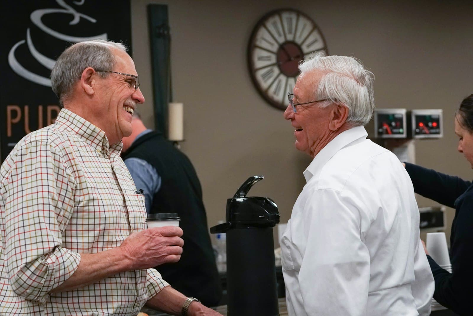 Two men laughing together over coffee in a church lobby